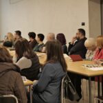 Sala konferencyjna. Osoby siedzące przy stołach.