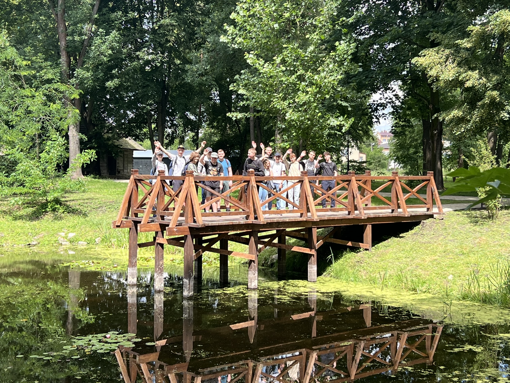 Małe molo drewniane nad jeziorem, a nim stoją uczniowie.