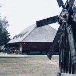 Widok na Muzeum Kultury Ludowej w Kolbuszowej. Na pierwszym planie drewniany wiatrak, w tle drewniana chata.