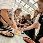 Grupa stojąca przy stole i przygotowująca pizzę
