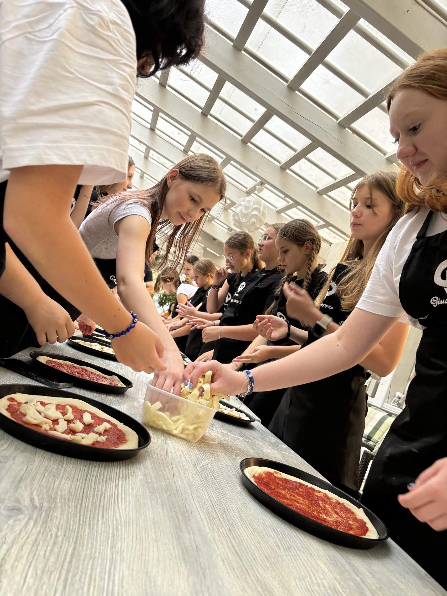 Grupa stojąca przy stole i przygotowująca pizzę