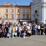 Grupa uczestników wizyty studyjnej na placu Niepodległości w Przemyślu. Za nimi fontanna, kamienica i wieża zegarowa