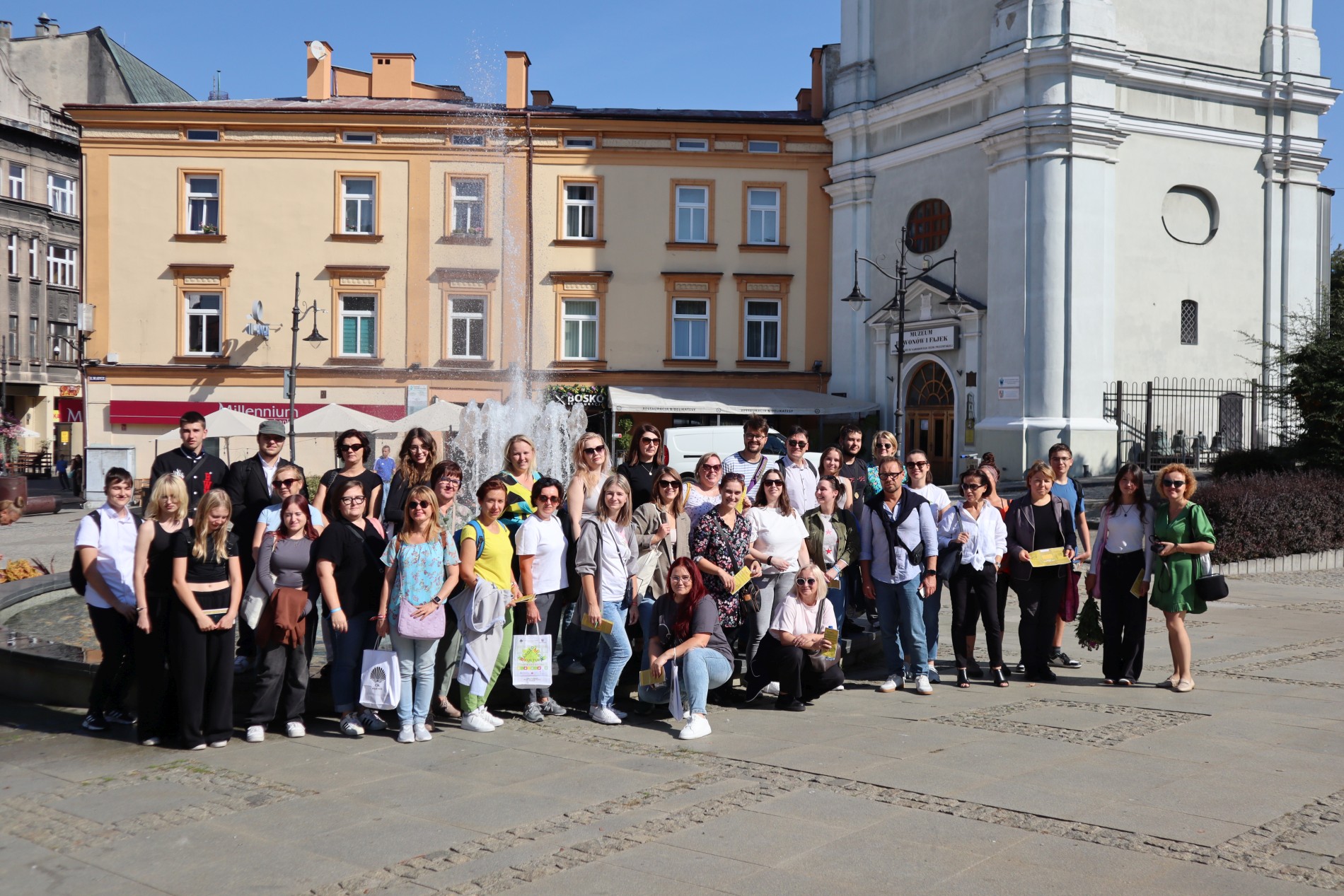 Grupa uczestników wizyty studyjnej na placu Niepodległości w Przemyślu. Za nimi fontanna, kamienica i wieża zegarowa